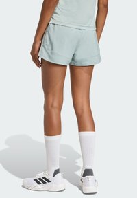 Light teal shorts with a smooth texture, featuring a relaxed fit and side seam pockets. Paired with white athletic socks and sneakers.