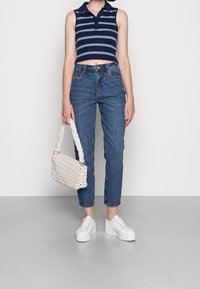Marinblå och vit randig cropped polo-shirt, blå högmidjade jeans, vit flätad handväska och vita plattformssneakers.