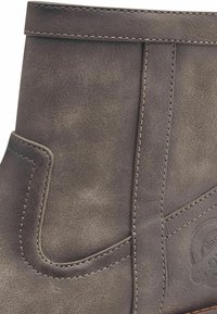 Bottine en cuir gris avec une finition texturée, des coutures renforcées et un détail de couture décoratif. Dispose d'un bout rond et d'un petit talon.