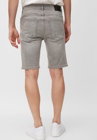 Pantalones cortos de mezclilla gris de corte regular, con dos bolsillos traseros, un dobladillo sin terminar y un ligero desvanecimiento, combinados con zapatillas blancas.