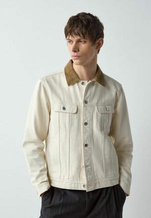 Cremefarbene Jeansjacke mit braunem Cordkragen, zwei Brusttaschen und silbernen Druckknöpfen, mit sichtbaren Nähten und figurbetontem Schnitt.
