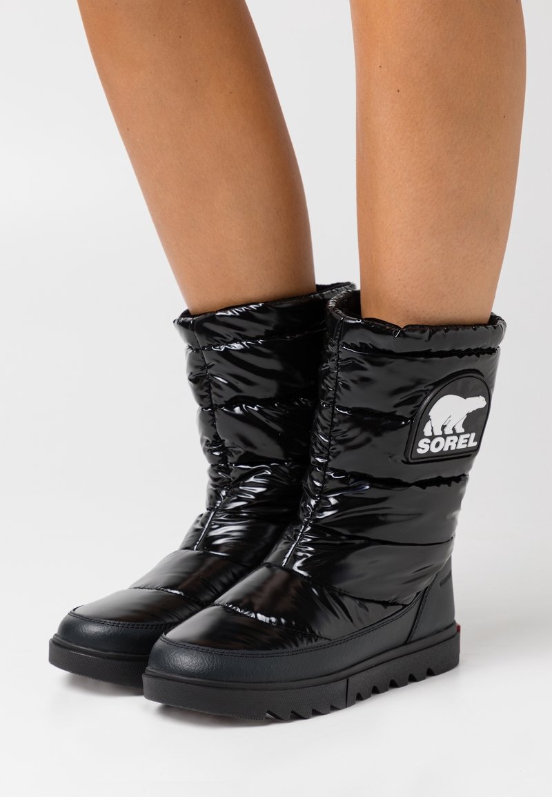 Stivali alla caviglia neri imbottiti con una finitura lucida, caratterizzati da una suola testurizzata e un patch rotondo con un orso polare.