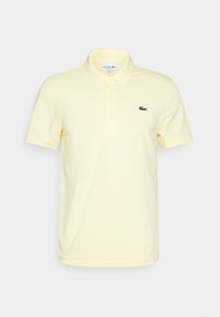 Světle žluté polo tričko vyrobené z bavlny, s klasickým límečkem, krátkými rukávy a malým zeleným logem Lacoste na levém prsu.