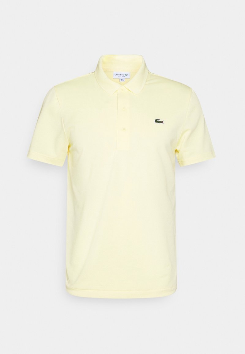 Světle žluté polo tričko vyrobené z bavlny, s klasickým límečkem, krátkými rukávy a malým zeleným logem Lacoste na levém prsu.
