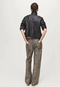 Veste courte en cuir noir avec un col montant, associée à un pantalon beige large imprimé léopard, mettant en valeur un tissu lisse et texturé.