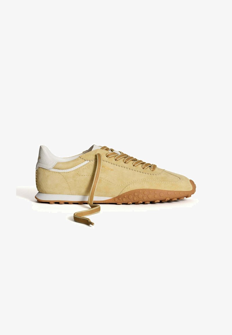 Sneakers en daim beige clair avec des accents en cuir blanc, bout rond et semelle en caoutchouc texturé. Dotés de lacets beiges et d'un col rembourré.