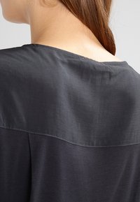 Top nero con una texture liscia e satinata nella parte superiore e un tessuto più morbido nella parte inferiore, con uno scollo semplice e arrotondato.