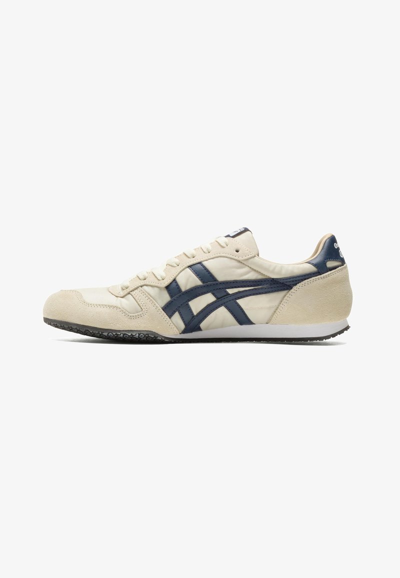 Baskets beiges à profil bas avec des rayures bleu marine, des lacets blancs, une semelle texturée et des accents en daim sur l'avant et le talon.