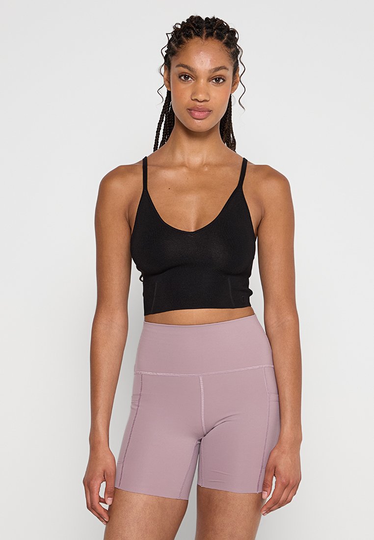 Top corto negro ajustado con tirantes finos, combinado con pantalones cortos rosa claro de tiro alto con costuras laterales y una textura suave.