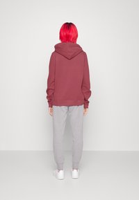 Sudadera burdeos con una capucha grande y puños acanalados, combinada con pantalones de chándal gris claro. El conjunto se completa con zapatillas blancas.