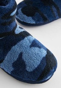 Blå og mørkeblå slippers i et blødt, tekstureret stof med et camouflage mønster, rund tå og lavskårne design.