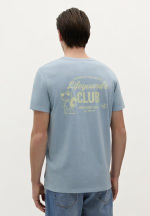 Lichtblauw katoenen T-shirt met een gele afbeelding op de achterkant, tekst "Lifeguard's Club" met een cartoonhond, korte mouwen en een ronde hals.