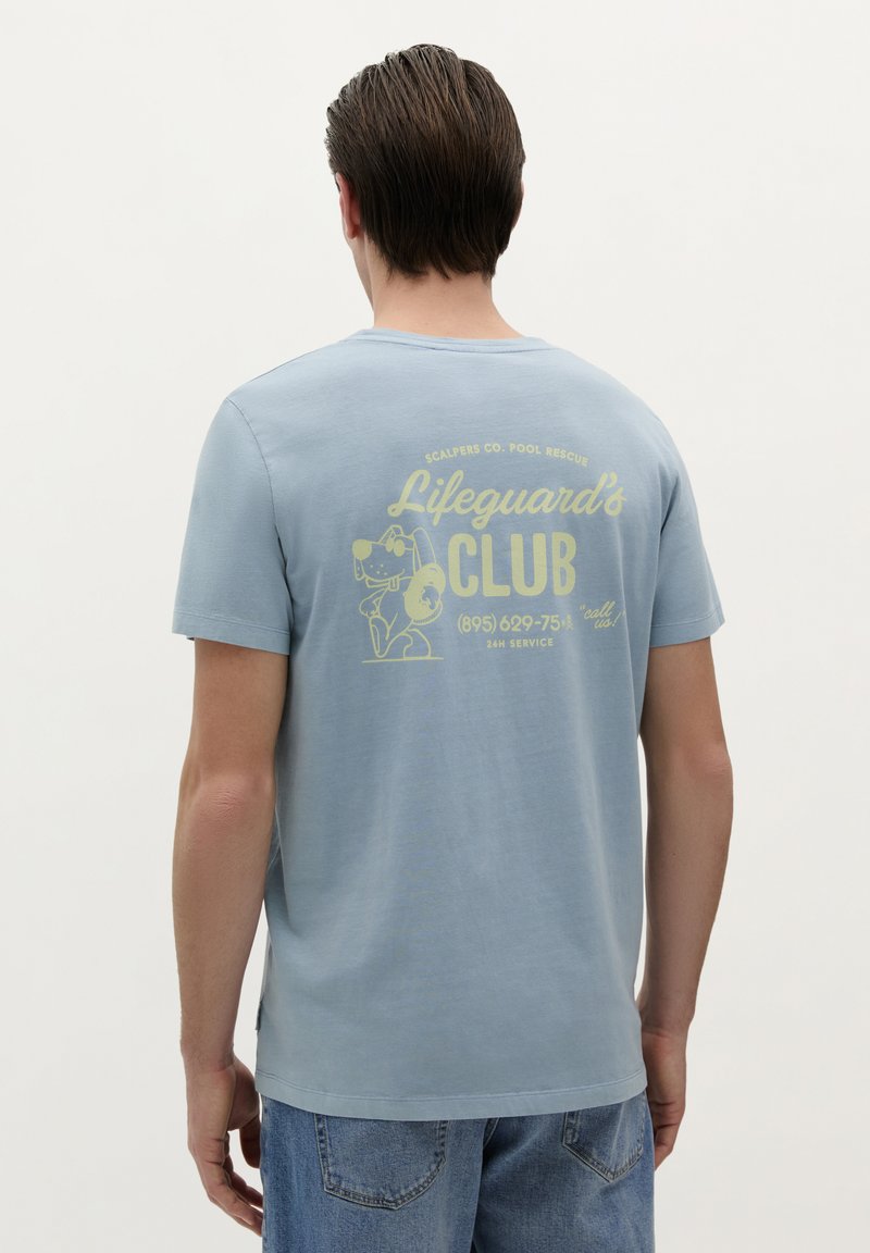 Lichtblauw katoenen T-shirt met een gele afbeelding op de achterkant, tekst "Lifeguard's Club" met een cartoonhond, korte mouwen en een ronde hals.