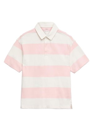 Młoda osoba stoi ze skrzyżowanymi ramionami, ubrana w różowo-białą koszulkę polo w paski, niebieskie szorty i białe trampki na jednolitym tle.