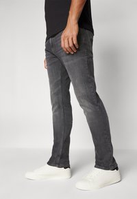 Vaqueros oscuros de corte Slim, fabricados en denim, con una textura suave, un ligero desgastado y detalles en las costuras laterales, combinados con zapatillas blancas.