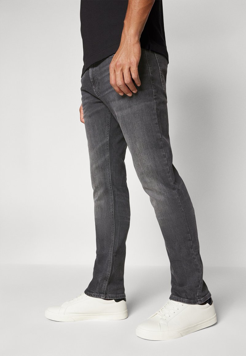 Vaqueros oscuros de corte Slim, fabricados en denim, con una textura suave, un ligero desgastado y detalles en las costuras laterales, combinados con zapatillas blancas.