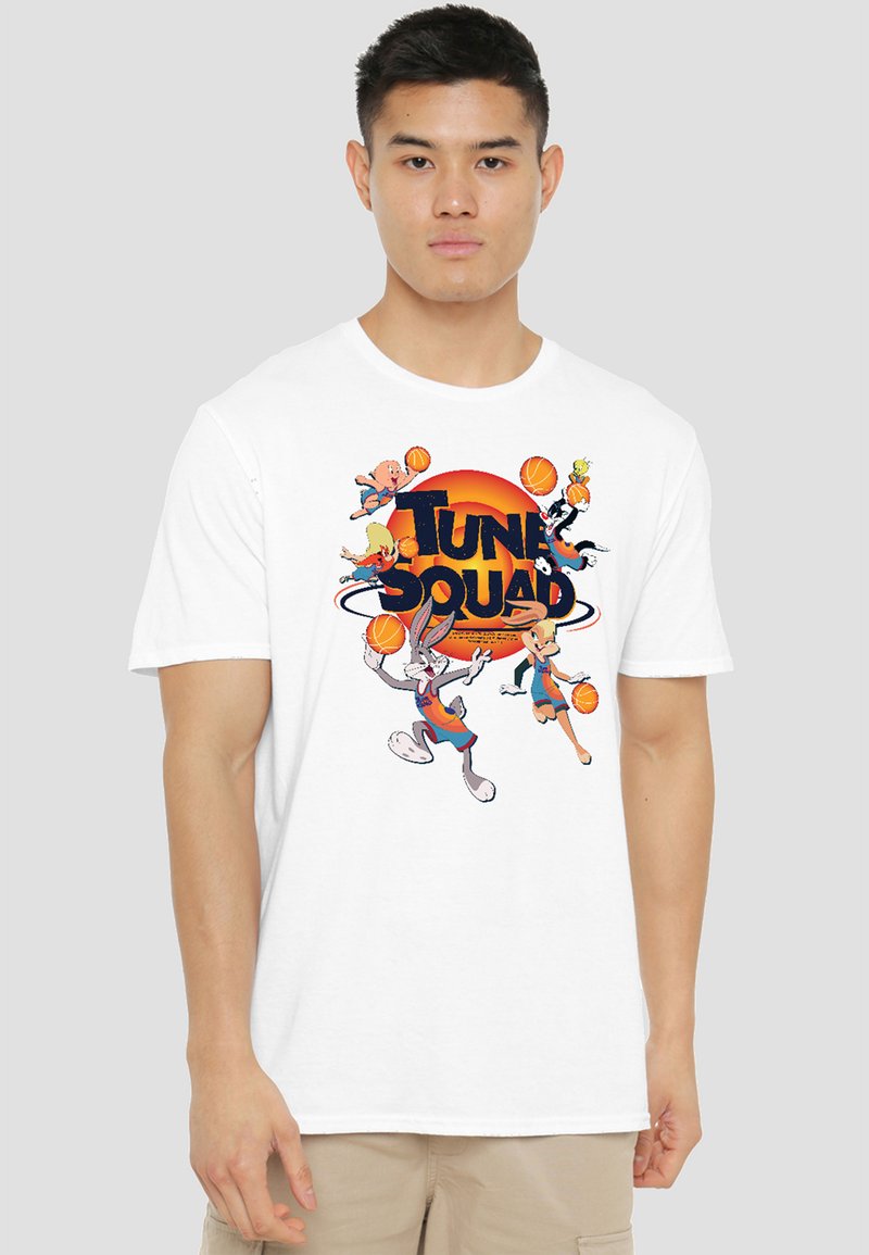 Young man wearing a white T-shirt with colorful "Tune Squad" text and basketball-playing cartoon characters from Looney Tunes.