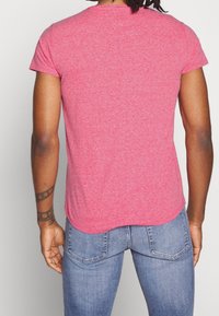 Tajt kortärmad t-shirt i melerad röd tyg, med rundad nederkant och en mjuk yta. Bärs med blå jeans.