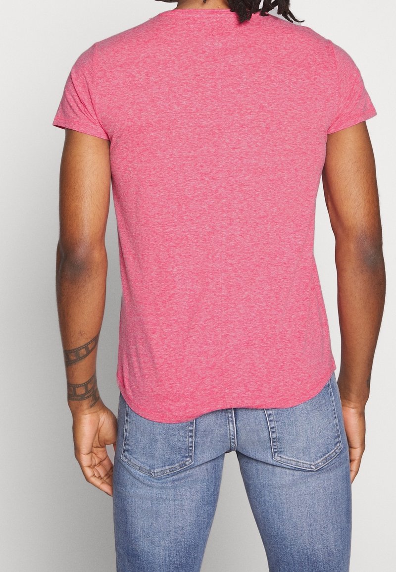 Tajt kortärmad t-shirt i melerad röd tyg, med rundad nederkant och en mjuk yta. Bärs med blå jeans.