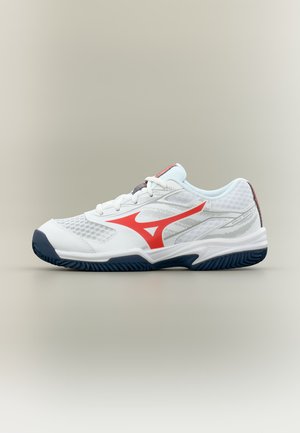 Chaussure de sport blanche avec logo rouge, semelle bleu marine et détails en mesh, vue de côté sur un fond clair uni.