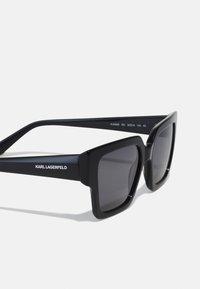 Occhiali da sole oversize neri con finitura opaca, montatura quadrata, lenti scure ombreggiate e il marchio "KARL LAGERFELD" sulla tempia.