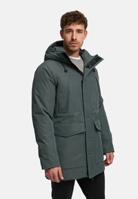 Mörkgrön isolerad parkas med huva, utrustad med en frontdragkedja, stora fickor och en texturerad tygfinish.