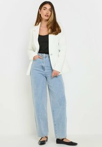 Blazer bianco testurizzato con bottone argento, canotta nera, jeans in denim azzurro chiaro a vita alta e scarpe basse nere.