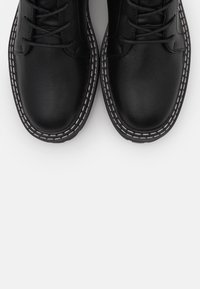 Scarpe in pelle nera con superficie liscia, dotate di chiusure con lacci e cuciture bianche a contrasto lungo la suola. Design classico con punta arrotondata.