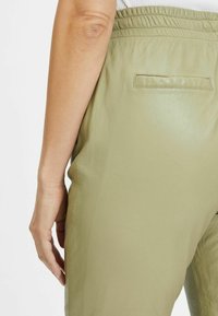 Groene leren broek met een gladde textuur, voorzien van een elastische tailleband en een enkele achterzak.