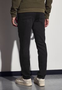 Pantalones negros de corte slim, confeccionados en un tejido texturizado. Presentan dos bolsillos traseros y se combinan con zapatillas color blanco roto.