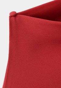 Tissu rouge avec un bord plié et un petit bouton rond recouvert de tissu dans le coin, montrant des détails de texture et de couture.