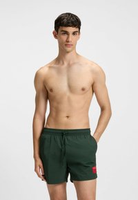 Costumi da bagno verdi con vita regolabile e un patch del logo rosso sul davanti. Realizzati in materiale leggero e a asciugatura rapida.