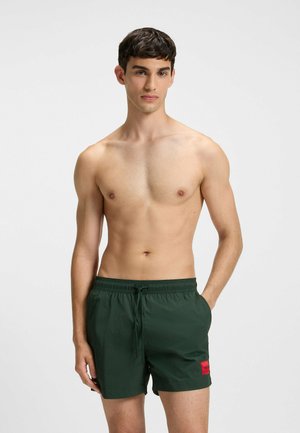 Groene zwembroek met een trekkoord in de taille en een rood logo op de voorkant. Gemaakt van lichtgewicht, snel drogend materiaal.