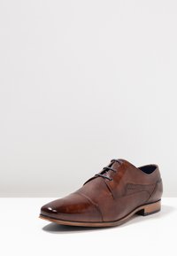 Zapato de cuero marrón con cordones, con un acabado liso y texturizado, punta afilada, cordones azules de contraste y un patrón sutil en la parte superior.