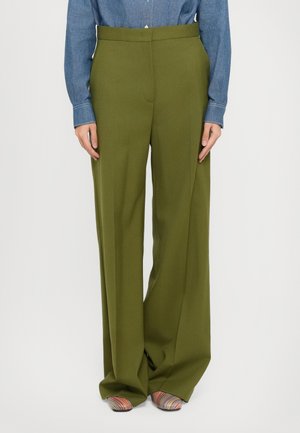 Pantalons larges verts en tissu lisse, dotés d'une taille haute et d'une coupe ajustée. Associés à une chemise en denim et des chaussures à motifs.