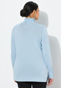 Hellblaues Langarmoberteil mit einem Rüschenausschnitt, gefertigt aus weichem Strickmaterial. Verfügt über seitliche Schlitze am Saum für mehr Bewegungsfreiheit.