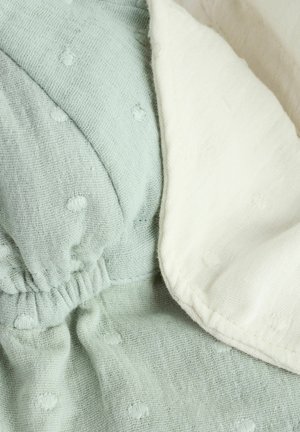 Tejido de algodón suave en verde menta claro y crema, con un patrón de puntos texturizados, detalles fruncidos y un borde doblado y liso.