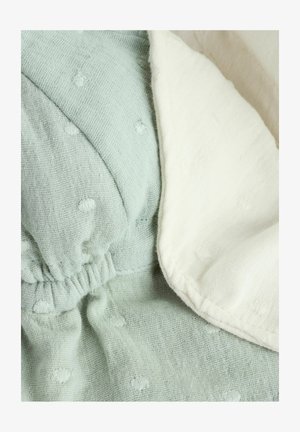 Mjukt bomullstyg i ljus mynta grön och krämvit, med ett strukturerat prickmönster, samlat detalj och en slät, vikt kant.