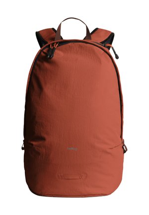 Sac à dos couleur rouille avec bretelles rembourrées noires, fermeture à double fermeture éclair, poignée de transport et logo discret à l'avant sur fond blanc.