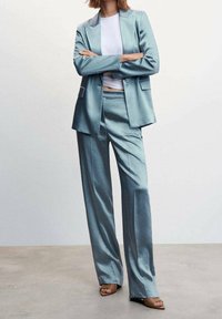 Himmelblaues Satinanzug mit einem taillierten Blazer und weiten Hosen, kombiniert mit einem weißen Oberteil und nude-farbenen Absätzen.