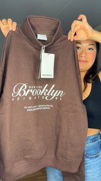 Barna cipzáras pulóver magas gallérral, fehér felirattal: "NEW YORK Brooklyn HEIGHTS 98" és Bershka címkével. Puha anyag.
