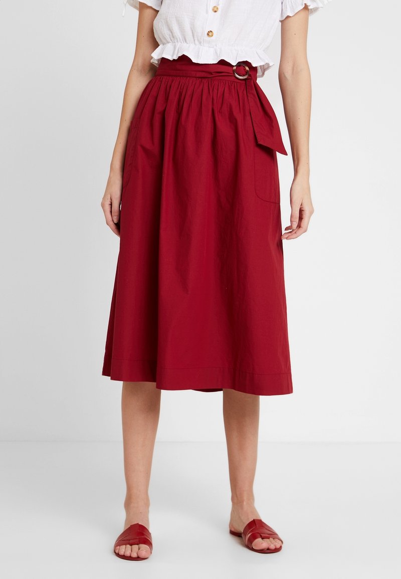 Czerwona, sięgająca do połowy długości spódnica z bawełny, z marszczonym pasem, boczną kieszenią oraz paskiem materiałowym z okrągłą klamrą.
