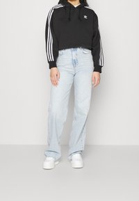 Svart kort hoodie med vita ränder på ärmarna, kombinerad med ljusblå högmidjade jeans och vita sneakers. Strukturerat tyg, avslappnad passform.