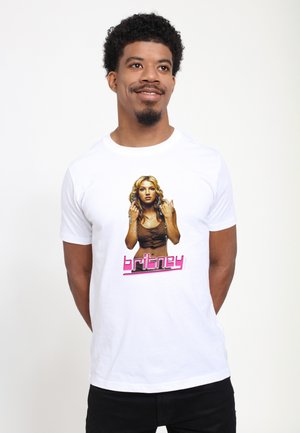 Uomo con capelli corti e ricci che sorride, indossa una T-shirt bianca con una foto e testo "britney" in rosa davanti.