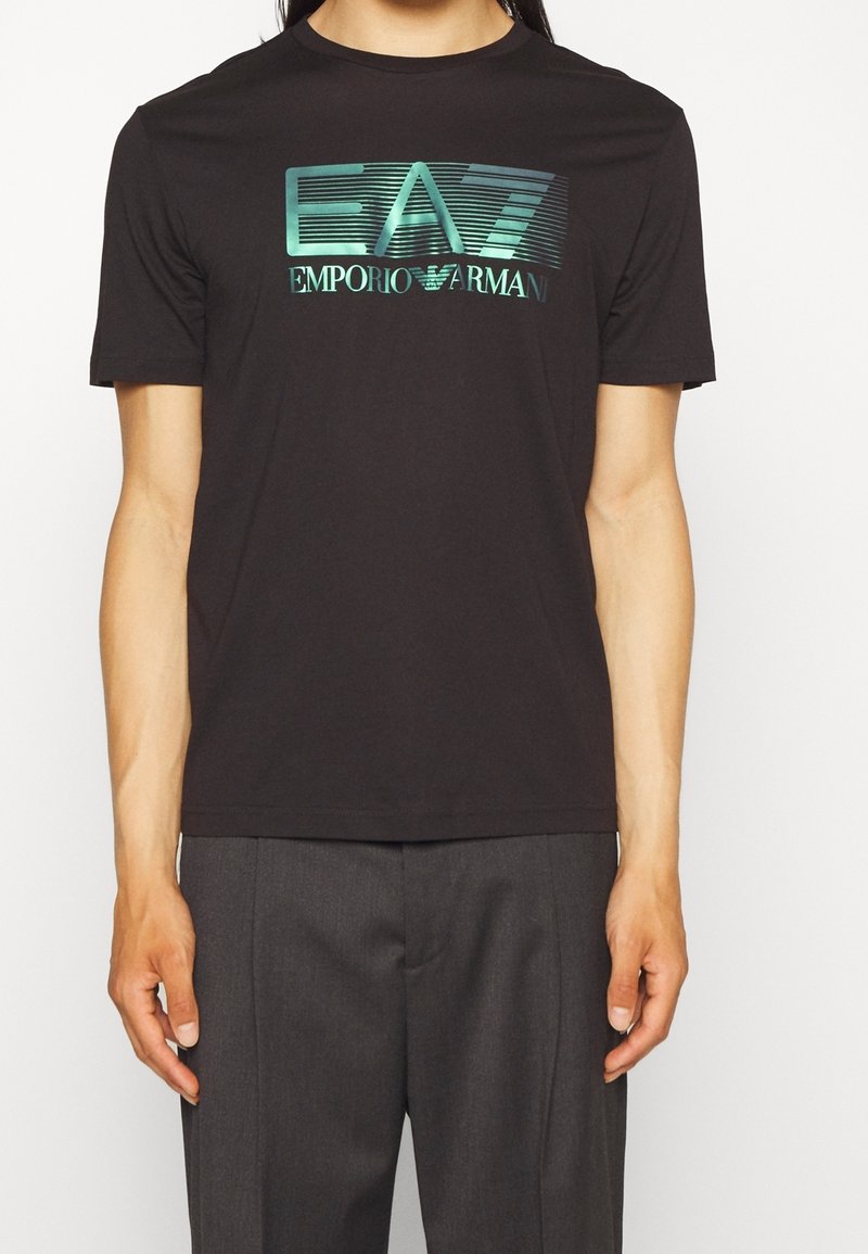 Svart bomullströja med en grafisk "EA7 EMPORIO ARMANI"-logotyp i turkos. Korta ärmar, rundad hals, slim fit-design.