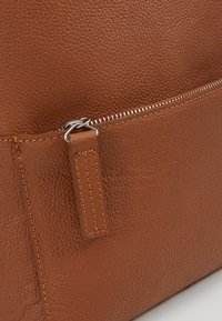 Sac à main en cuir marron avec une finition texturée, doté d'une fermeture éclair en argent et d'une tirette en cuir rectangulaire cousue sur le côté.
