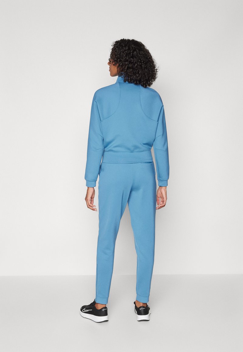 Abbigliamento athleisure blu composto da un top con zip a collo alto e pantaloni aderenti abbinati. Tessuto liscio con dettagli a coste sui polsini e sulle caviglie.