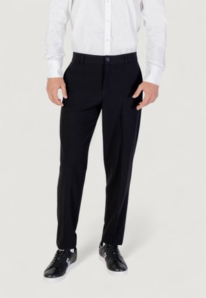 Pantalones de vestir negros hechos de tela suave con un ajuste entallado, con cierre de botón y bolsillos laterales, combinados con zapatillas negras.