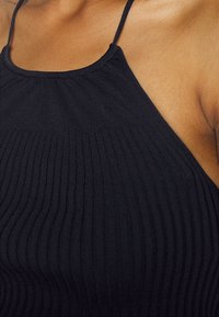Top de alças finas, preto, com um padrão canelado, apresentando uma superfície texturizada e uma silhueta ajustada. Tecido suave com um ligeiro brilho.