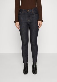 Jeans skinny de mezclilla oscura con un talle medio, que presentan cinco bolsillos, costuras a tono y se combinan con botas negras hasta el tobillo.